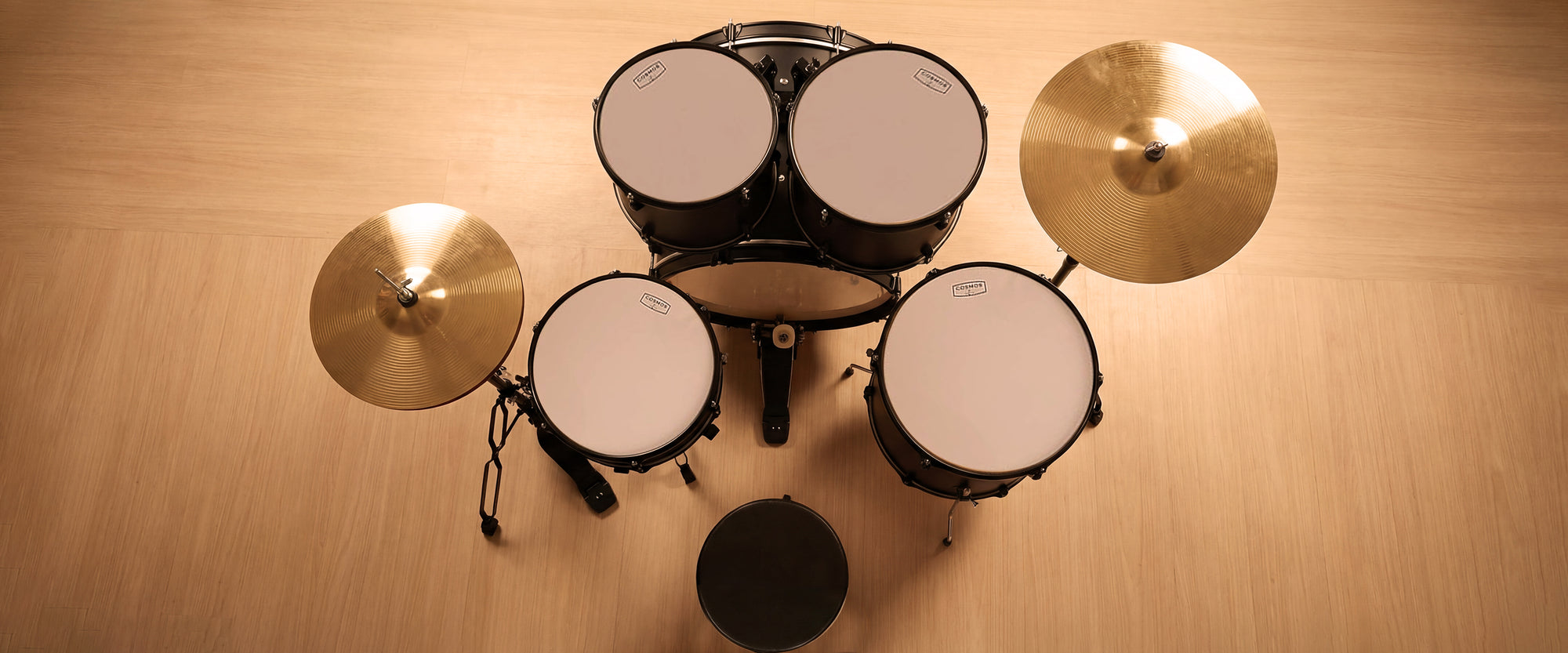 Desktop banner side profile view of a black 5-piece drum kit, focusing on the durability of the double-braced stands and bass drum spurs.