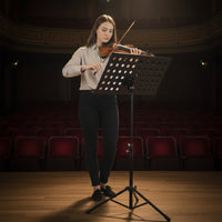Woman playing violin on a stage with a music stand in an auditorium