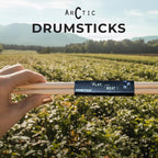 Drumsticks held by a hand with 'Arctic Drumsticks' branding against a scenic background.
