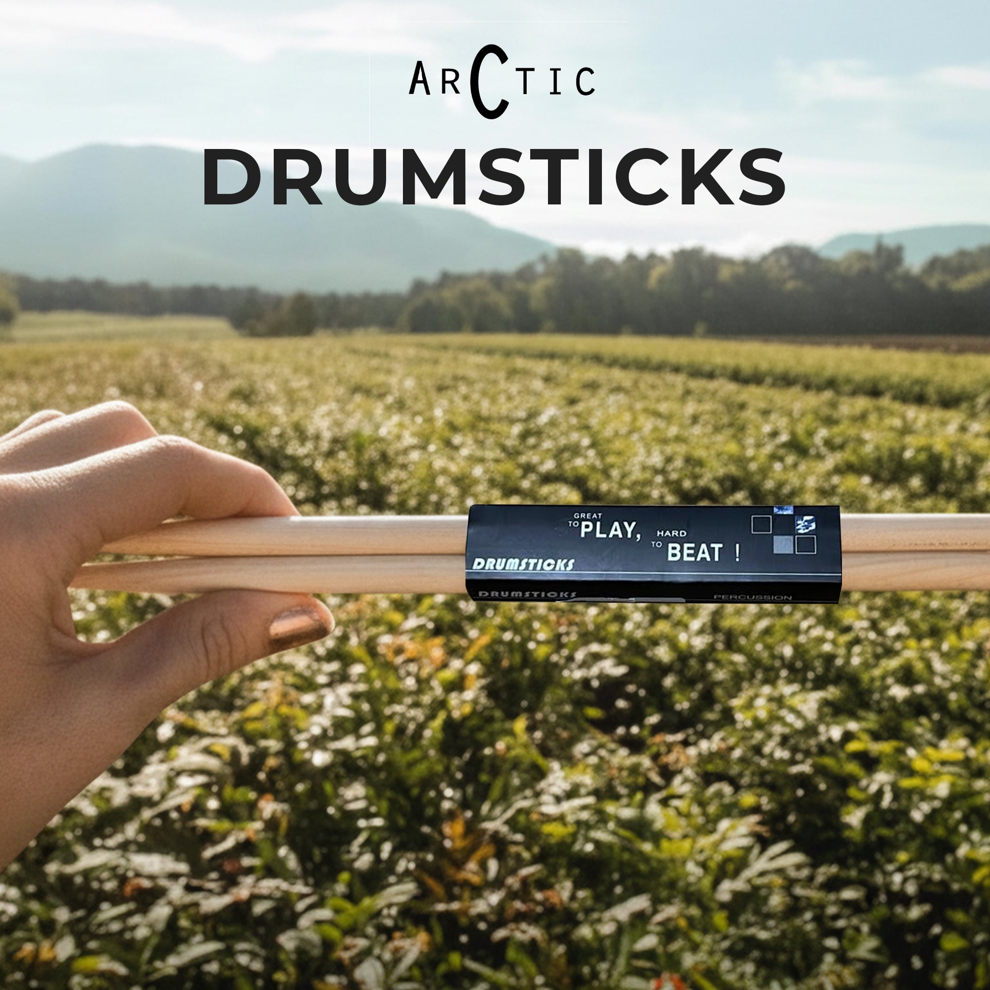 Drumsticks held by a hand with 'Arctic Drumsticks' branding against a scenic background.
