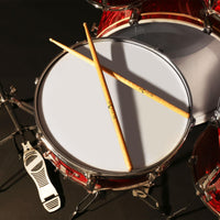 Close-up of a drum set with a snare drum, hi-hat, and drumsticks on a dark background.