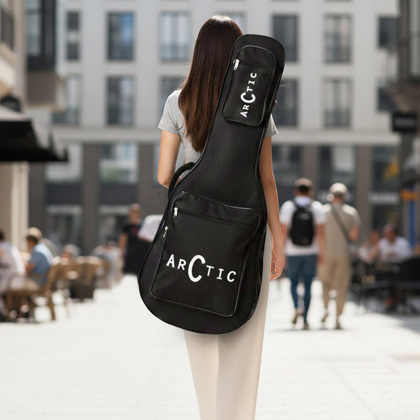 Person carrying a black guitar case with 'Arctic' branding on a city street.